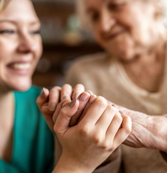 A young nurse and senior woman holding hands.